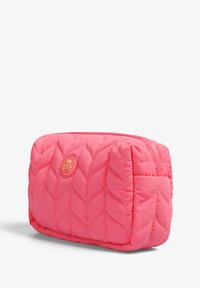 Neceser acolchado de color rosa con un patrón de hojas, forma redondeada, cierre superior con cremallera y un pequeño emblema de calavera en la parte frontal.