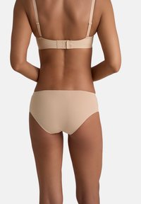 Donna che indossa un reggiseno beige senza cuciture e mutandine abbinate, mostrata di spalle su uno sfondo bianco uniforme.