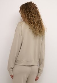 Beige sweatshirt with loose fit, dropped shoulders, and ribbed hem. Soft fabric, no patterns or hardware visible. Back view of garment.
