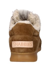 Bruin suède sneaker met een lichtbeige bontvoering. Heeft een tan rubberen zool en een zichtbaar merklabel op de achterkant gestikt.