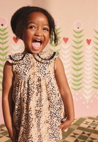 Leoparda raksta kleita ar volānveida apkakli, pogu priekšpusi un izplatu svārku. Dabīgs audums ar dažādu brūnu, krēmkrāsu un dzeltenu toņu kombināciju.