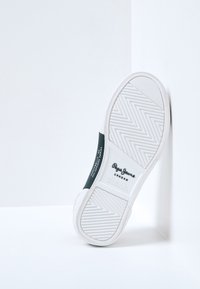 Biała gumowa podeszwa sportowa z wzorem w jodełkę, z czarnym akcentem i oznaczeniem marki na boku. Czysty, minimalistyczny design.