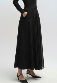 Falda maxi plisada negra con bolsillos laterales, hecha de tela ligera, con una cintura ajustada y una textura suave y fluida.