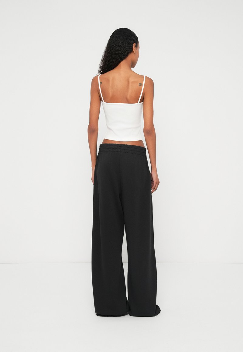 Top corto blanco sin mangas con tirantes finos, combinado con pantalones deportivos negros de corte holgado y cintura elástica. Textura suave, diseño minimalista.