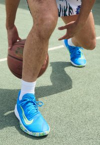 Blue athletic shoes with a textured upper and patterned sole. The design features bright yellow accents and laces. A basketball is in motion.
