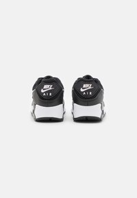 Fekete és fehér Nike Air sportcipők, texturált felsőrésszel, párnázott bokarészes kialakítással és hangsúlyos márkázással a sarkon. Klasszikus fűzős dizájn.