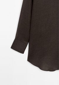 Długi, ciemnobrązowy lniany rękaw koszuli z mankietem i zaokrąglonym dolnym brzegiem na białym tle.