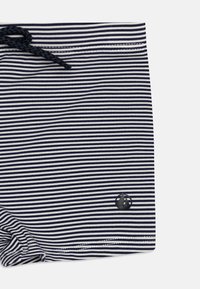 Costume da bagno a righe blu navy e bianche con vita regolabile tramite cordoncino e un piccolo logo di una barca a vela nera nell'angolo in basso a destra. Texture liscia.