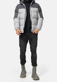 Doudoune grise et gris foncé, dotée d'une capuche, d'un design matelassé, de poignets élastiques, associée à un jean foncé et des bottes zippées grises.