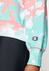 Felpa tie-dye verde menta e rosa con polsini a coste, caratterizzata da un piccolo logo ricamato sulla manica. Tessuto morbido.