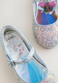 Glitzernde silberne Mary Jane-Schuhe mit einer Schnalle, die bunte Muster von Prinzessinnen auf den Innensohlen zeigen, strukturiert mit mehrfarbigem Glitzer.