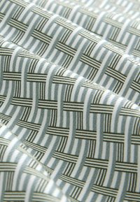 Zbliżenie na jasnokolorową tkaninę z geometrycznym, czarno-szarym wzorem tkanym, tworzącym przecinające się linie poziome i pionowe.