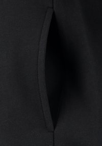Tela negra que muestra un detalle de bolsillo vertical. El material tiene una textura suave con un ligero estiramiento. Diseño simple y funcional.