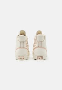 Wysokie sneakersy z kremowego płótna, różowe przeszycia, okrągła naszywka z logo na pięcie oraz gumowa podeszwa. Minimalistyczny design bez sznurówek.