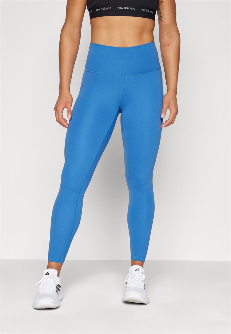 Mallas de cintura alta azules, textura suave, material elástico, con un diseño ajustado. Combinadas con zapatillas deportivas blancas.