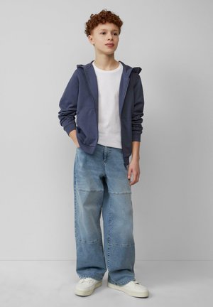 Marineblauwe ritscrewneck hoodie met kangoeroezakken over een wit T-shirt; gecombineerd met losse lichtblauwe jeans met stiknaaddetails en witte sneakers.