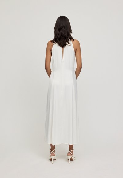 Vestido midi blanco con un detalle de espalda con ojal, textura suave y silueta fluida, combinado con tacones blancos con tiras.