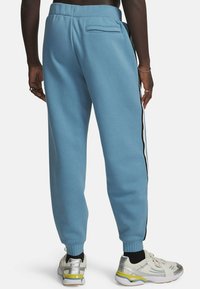 Blauwe joggingsbroek met een ontspannen pasvorm, voorzien van enkelboorden, een achterzak en zwart-witte zijstrepen. Zacht materiaal met een gladde textuur.