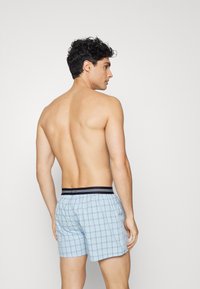 Boxers en vichy bleu avec une ceinture élastique noir et blanc, montrant un dos et des épaules lisses. Pas d'autres caractéristiques visibles.