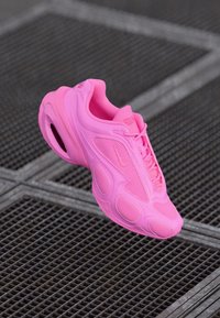 Pink Nike sneaker featuring a mesh upper, textured accents, a rounded shape, and a visible air cushioning unit in the sole.
