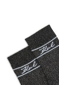 Čierne ponožky s textúrovaným vzorom. Obsahujú biely pruh a logo 'Hel' pozdĺž oblasti lemu. Materiál sa zdá byť mäkký a pletený.