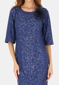 Granatowa sukienka z cekinami, krótkimi rękawami, teksturowaną tkaniną oraz akcentem z futerka na ramieniu. Charakteryzuje się dopasowanym krojem.