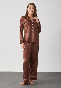 Ensemble de pyjama en satin à rayures brunes comprenant une chemise à boutons et un pantalon long. Présente des garnitures blanches sur le col et les poignets du pantalon. Texture lisse.