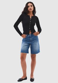 Svart ribbad långärmad topp med knäppning och denim Bermuda-shorts. Modellen bär svarta ballerinas; shortsen har fransade kanter och en klassisk passform.
