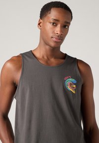 Débardeur gris sans manches en coton avec un col rond. Présente un logo "Levi's" coloré et un graphisme de vague avec un design stylisé.