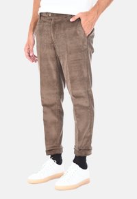 Pantaloni in corduroy marroni, con texture a righe verticali, tasche anteriori e gamba leggermente affusolata. Indossati con sneakers bianche e calze nere.