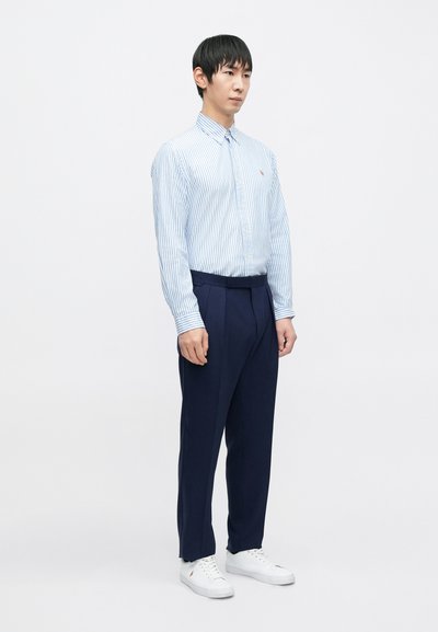 Camisa de botão azul claro com riscas brancas, calças azul-marinho e sapatilhas brancas. Tecido fino, corte descontraído e pequeno detalhe de logótipo na camisa.