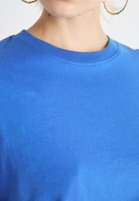 Camiseta azul brillante con cuello redondo, textura suave y mangas cortas, que presenta sutiles detalles de costura alrededor del escote.