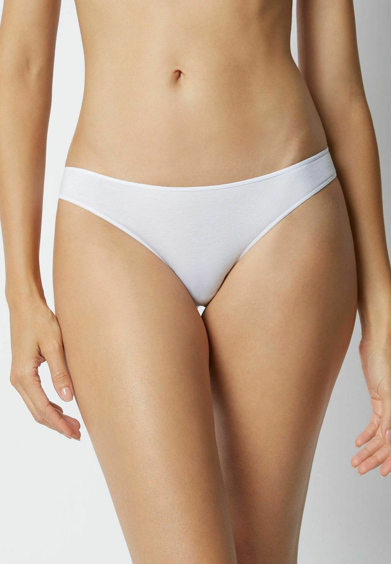 Bílé bavlněné bikiny s hladkou texturou, nízkým střihem a minimálním elastickým pasem, které ukazují čistý a jednoduchý styl.