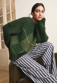 Forest green, fuzzy sweater with a diamond pattern in a lighter green hue. Paired with navy and white striped wide-leg pants.