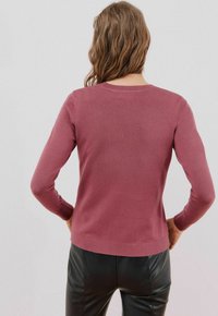 Maglione a maniche lunghe color malva, realizzato in morbido materiale a maglia. Presenta un collo rotondo e un orlo a coste, abbinato a pantaloni in pelle nera.