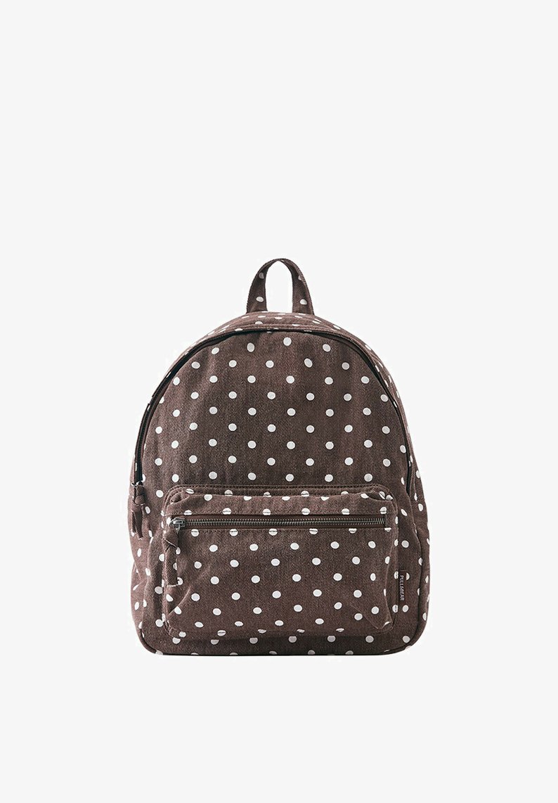 Sac à dos en tissu marron à pois blancs, avec une poche avant zippée et une poignée supérieure sur fond blanc.