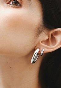 Pendientes de aro de plata, uno de diseño grande y liso y otro delgado con superficie texturada, que muestran acabados pulidos y reflectantes.