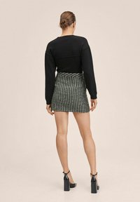 Maglione nero accorciato abbinato a una gonna a scacchi in bianco e nero, con una silhouette attillata. La modella indossa scarpe nere con tacco squadrato.