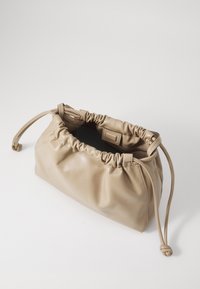 Beige lær clutch-veske med samlet topp, snøring og glatt tekstur. Åpen design avslører et enkelt mørkt interiør.