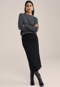 Pulover gri din lână cu mâneci lungi, combinat cu o fustă neagră ajustată cu o fente pe lateral. Purtați cu cizme din piele negre până la genunchi.