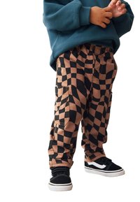 Cargo nohavice so vzorom hnedo-čiernej šachovnice a bočnými vreckami, doplnené čiernymi teniskami s bielymi detailmi a čiernym šnurovaním.