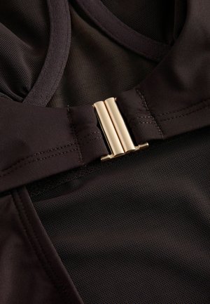 Sort atletisk beklædningsgenstand med en øverste del i mesh og en glat nederste del. Detalje med guldfarvet lukning. Tekstureret stof synligt.