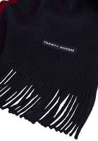 Donker marineblauwe gebreide sjaal met franjes aan de uiteinden en een Tommy Hilfiger logo patch in het midden.