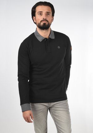 Crna majica s dugim rukavima i golfer kragnom u sivoj boji, s dugmetima na prednjem dijelu i logotipom na prsima, te smešnim zakrpama na rukavu.