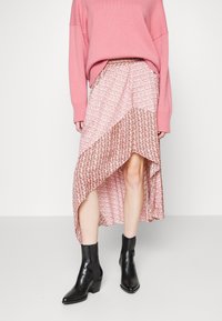 Rosa Pullover über einem gemusterten, asymmetrischen Rock mit floralen Designs und einem geometrischen unteren Abschnitt, kombiniert mit schwarzen Knöchelstiefeln.