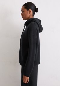 Czarna bluza z kapturem wykonana z miękkiego materiału, z szerokimi rękawami i luźnym krojem, zestawiona z czarną, prążkowaną spódnicą.