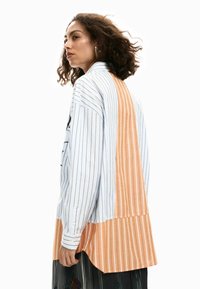 Triibuline nööpidega särk, millel on sinise ja valge vertikaalse triibumustriga, oranži triibulise tagapaneeliga ja lõdva lõikega.