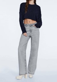 Pull court en maille bleu marine avec motif texturé, associé à un jean gris clair taille haute, ample, et des chaussures à plateforme.