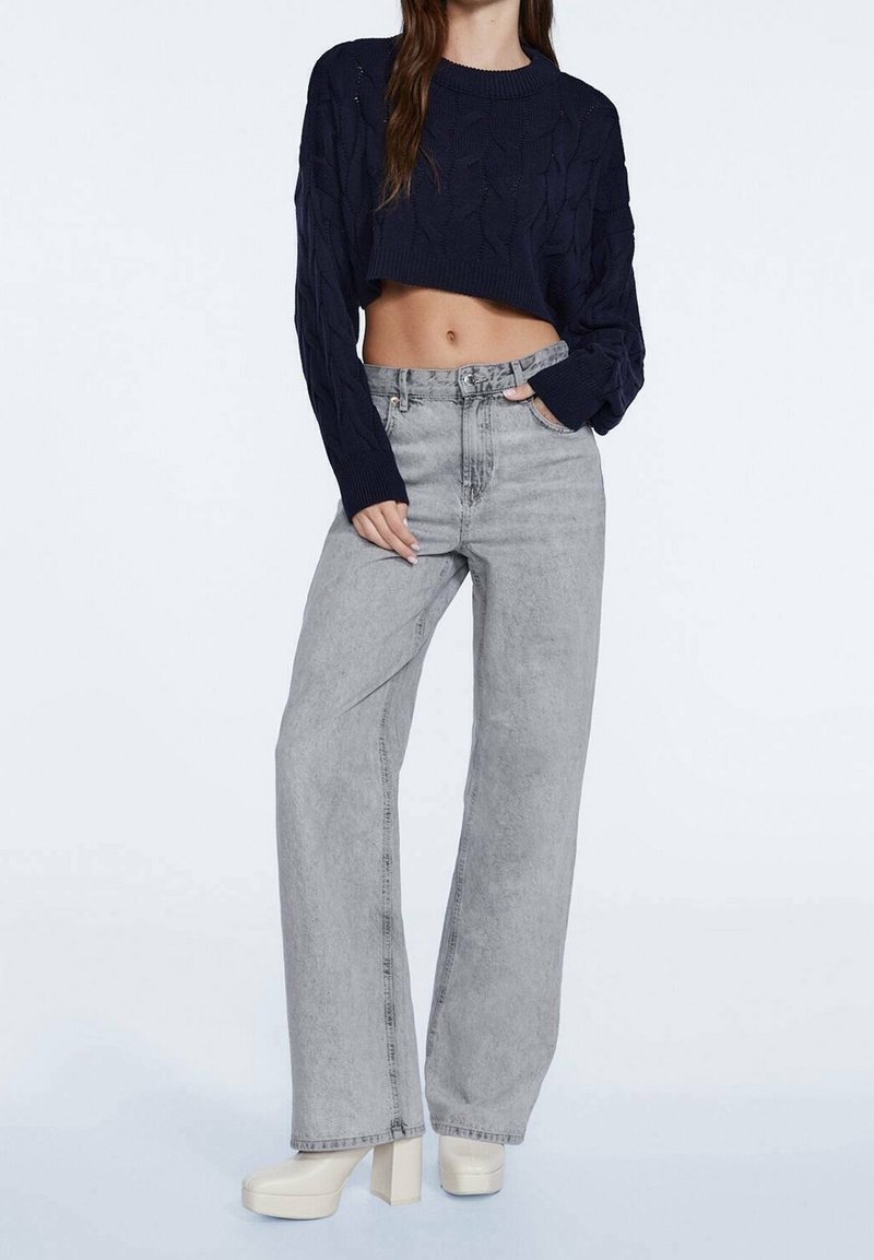 Pull court en maille bleu marine avec motif texturé, associé à un jean gris clair taille haute, ample, et des chaussures à plateforme.