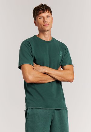 Green cotton t-shirt with short sleeves, crew neckline, and a subtle logo on the left chest. Smooth texture with stitched edges.